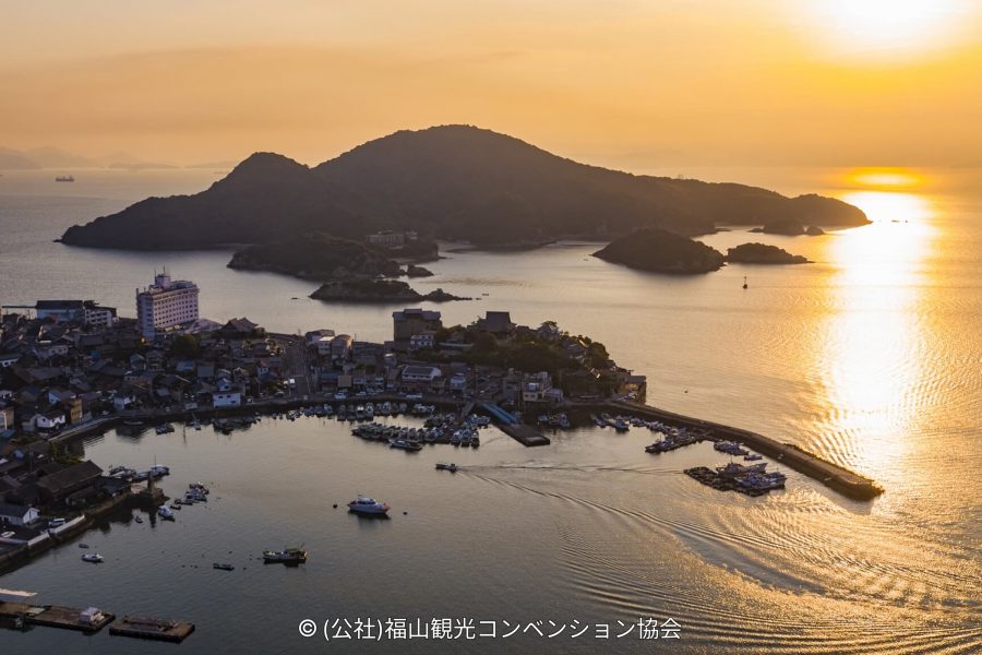 Aerial view of the Tomonoura harbor and the surrounding landmass silhouetted against a brilliant sunset over the Seto Inland Sea.