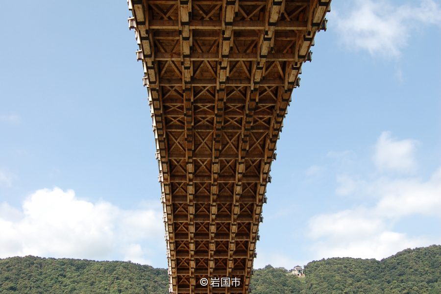 An extreme low-angle view from the river up into the complex wooden structure and joinery beneath one of the Kintai Bridge arches.