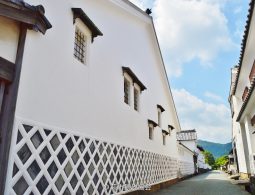 The preserved streetscape of Hagi Castle Town, featuring a large white earthen wall with a diamond-patterned namako-kabe base under a blue sky.
