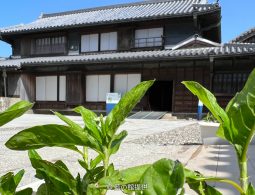 The facade of the traditional wooden machiya-style Okumura Family Residence, viewed over a foreground plant.