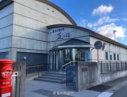 The modern exterior of the Ai no Yakata building with a curved roof and an old red mailbox in the foreground.