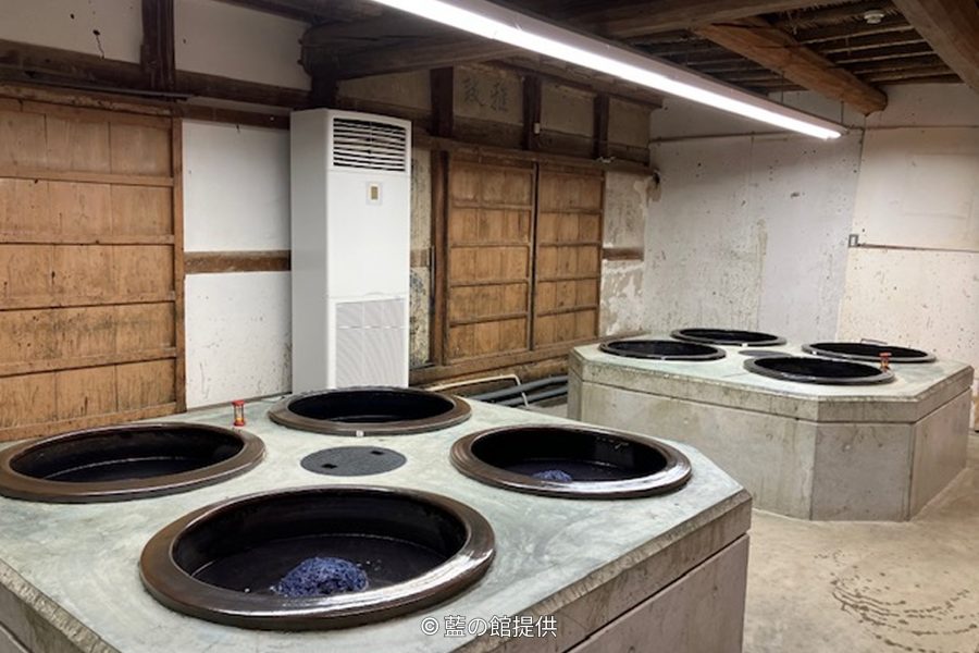 The interior of the traditional indigo dyeing workshop (Nedoko) with concrete vats containing deep blue indigo dye.