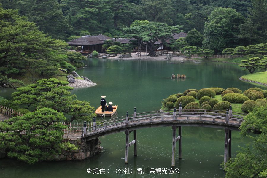 The Engetsukyo (Crescent Moon Bridge) arching over a pond in Ritsurin Garden, with a small boat nearby, surrounded by lush green foliage.