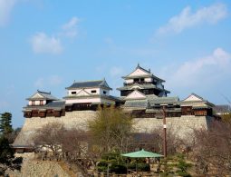 The main keep and connected turrets of Matsuyama Castle, with white walls and dark roofs, standing on a large stone wall.