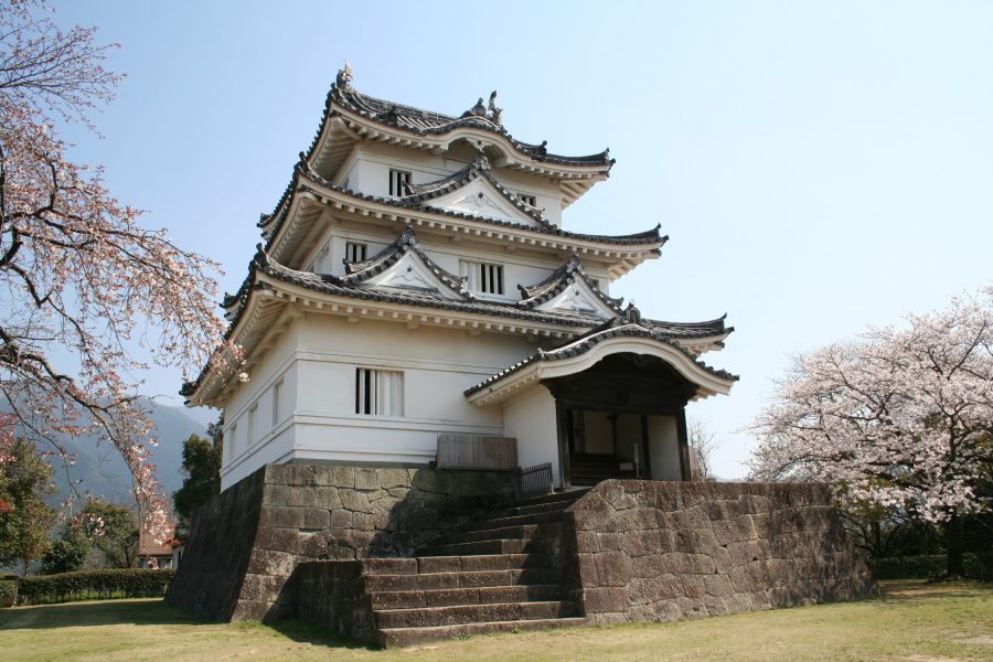 The white, three-tiered main keep of Uwajima Castle, one of Japan's original castles, built on a stone base and surrounded by cherry blossoms.