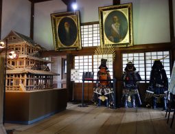 The white, three-tiered main keep of Uwajima Castle, one of Japan's original castles, built on a large stone base and flanked by blooming cherry trees in spring.