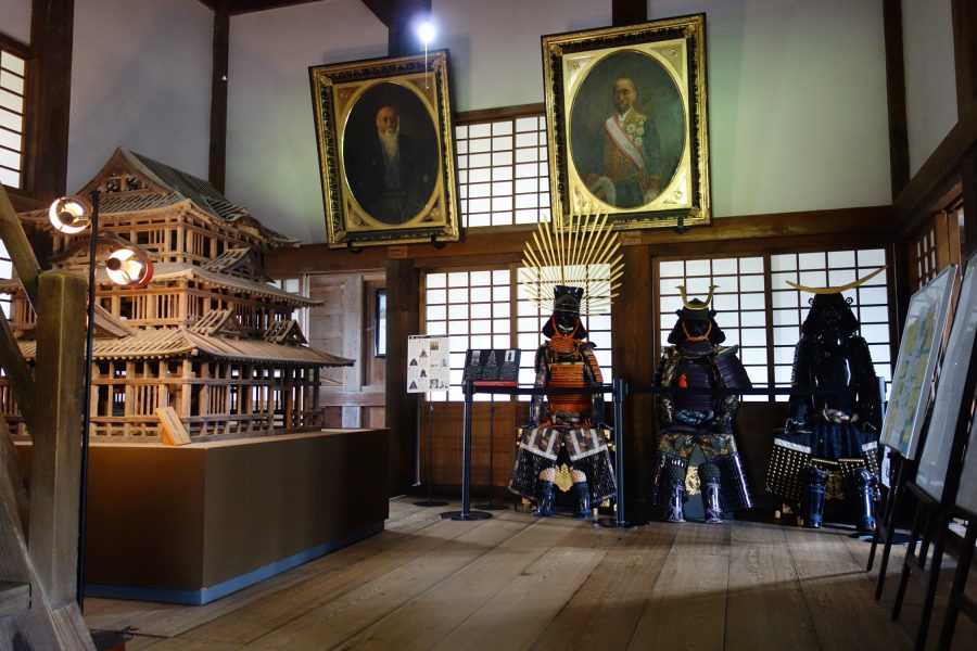 The white, three-tiered main keep of Uwajima Castle, one of Japan's original castles, built on a large stone base and flanked by blooming cherry trees in spring.