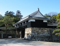 The Kuroganemon Gate (or similar turret gate) of Kochi Castle on its stone foundation, with the main keep visible on the hill behind it.