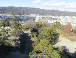 A view from the Kochi Castle walls overlooking the city and surrounding mountains, showing a stone staircase and park area in the foreground.