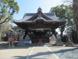 The main hall of a shrine (likely Fukushima Hachimangu) with a tiled roof and a stone approach, flanked by guardian dog statues.