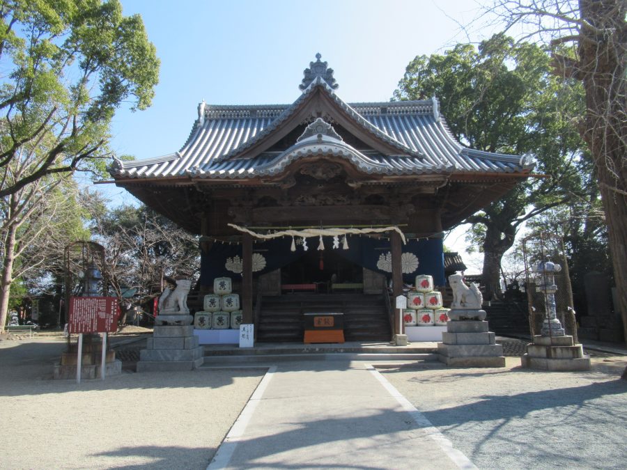The main hall of a shrine (likely Fukushima Hachimangu) with a tiled roof and a stone approach, flanked by guardian dog statues.