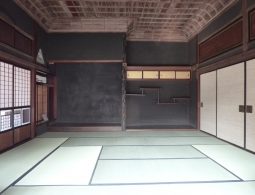The interior of a traditional Japanese room in a preserved merchant residence, featuring tatami mats, dark wood paneling, and a decorative ceiling.
