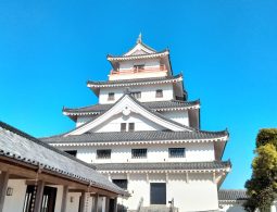 The main keep of Karatsu Castle, featuring white walls and dark tiled roofs, viewed from the courtyard under a bright blue sky.