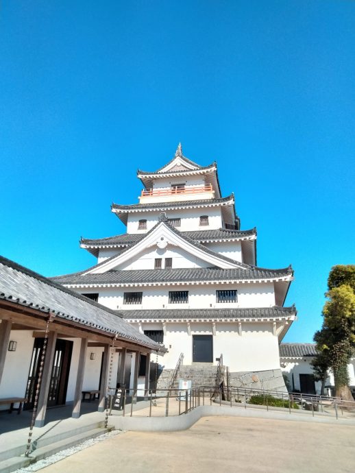 The main keep of Karatsu Castle, featuring white walls and dark tiled roofs, viewed from the courtyard under a bright blue sky.