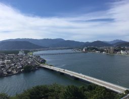 A panoramic view from Karatsu Castle overlooking the city, rivers, and mountains under a blue, cloudy sky.