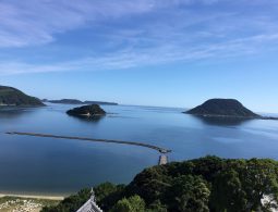 A high-angle view from Karatsu Castle overlooking the calm blue sea, small islands (likely Taka-shima), and a winding breakwater.