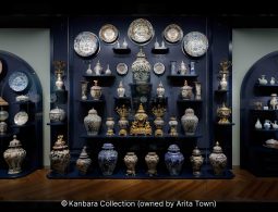 An elaborate museum display of colorful Japanese and export porcelain, plates, and vases against a dark blue background.