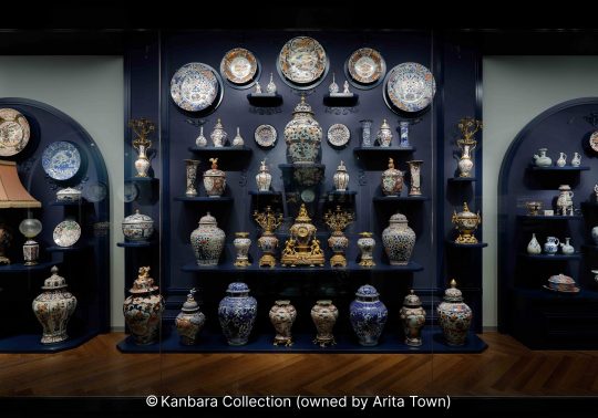 An elaborate museum display of colorful Japanese and export porcelain, plates, and vases against a dark blue background.