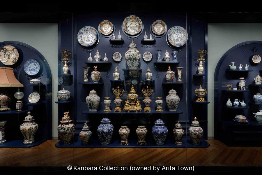 An elaborate museum display of colorful Japanese and export porcelain, plates, and vases against a dark blue background.