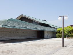 The modern exterior of the Kyushu Ceramic Museum building with a wide, tiled roof and light-colored brick walls.