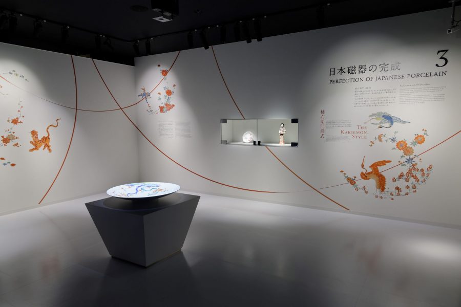 A modern, brightly lit museum exhibit dedicated to the Kakiemon style of porcelain, featuring a small porcelain doll and a plate on a pedestal.