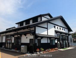 The renovated Hirado Tourist Information Center building, featuring traditional black and white dozo-style architecture, with the castle visible on the hill in the distance.