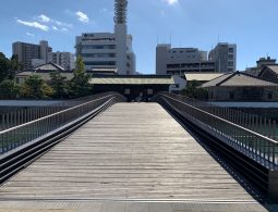 The illuminated wooden bridge connecting the historic Dejima Island to the modern city at dusk, with the word "dejima" written in Japanese characters.