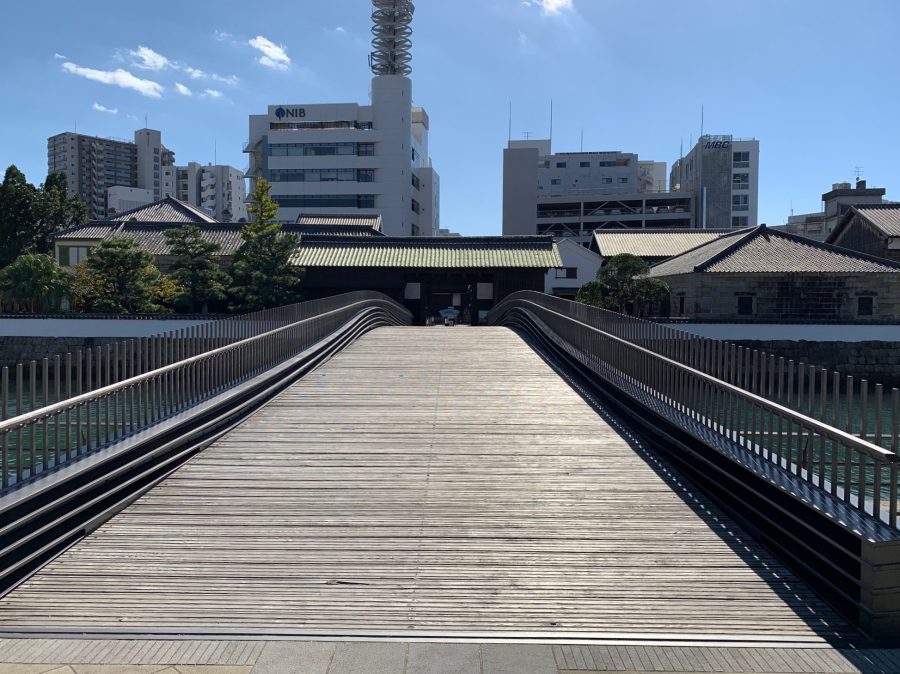 The illuminated wooden bridge connecting the historic Dejima Island to the modern city at dusk, with the word "dejima" written in Japanese characters.