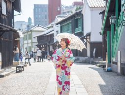 A woman in a colorful kimono holding a parasol walking along the cobblestone street in the reconstructed Dejima area.