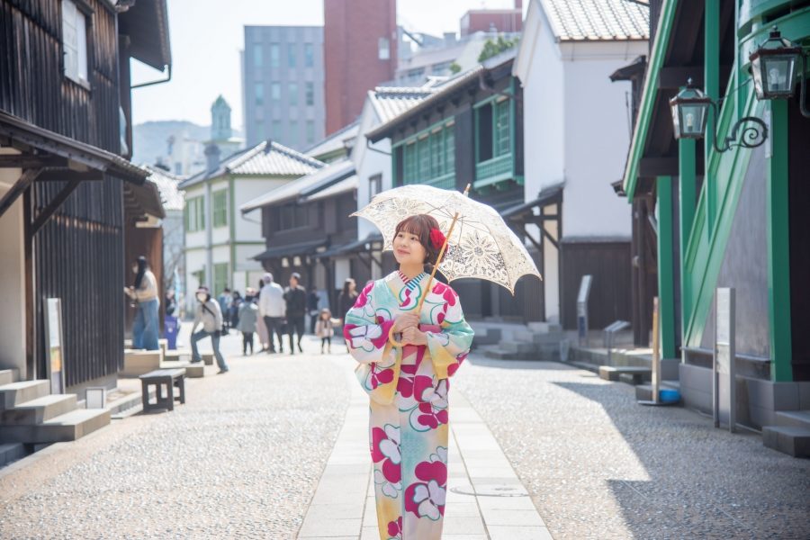 A woman in a colorful kimono holding a parasol walking along the cobblestone street in the reconstructed Dejima area.