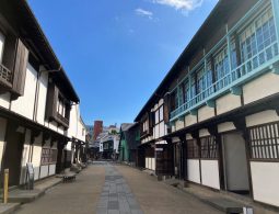 The preserved streetscape inside Dejima, lined with reconstructed traditional buildings featuring white walls and dark wood, with bright blue accents.