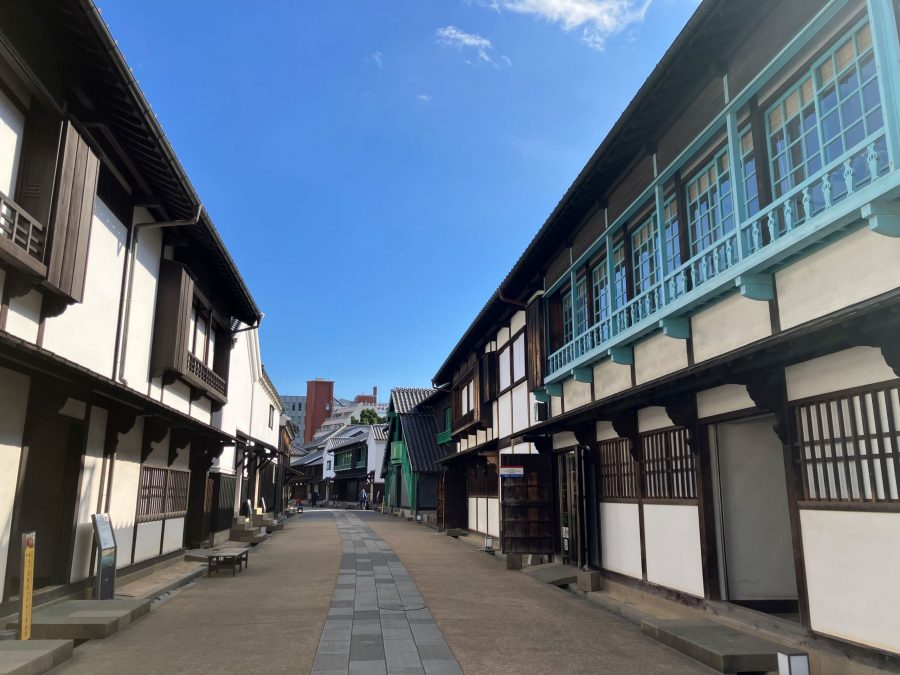 The preserved streetscape inside Dejima, lined with reconstructed traditional buildings featuring white walls and dark wood, with bright blue accents.