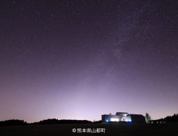 A wide shot of a modern building and distant lights under a dark night sky filled with countless stars.