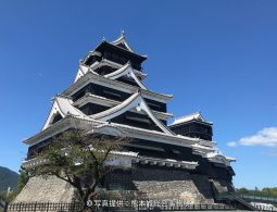 The reconstructed main keep of Kumamoto Castle with black wooden siding and white plaster, rising above its stone walls on a bright, sunny day.
