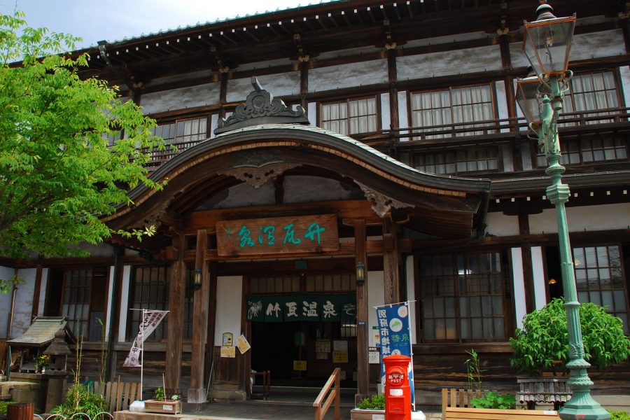 The main entrance facade of Takegawara Onsen, featuring traditional Japanese wooden architecture, like its curved karahafu gable roof.