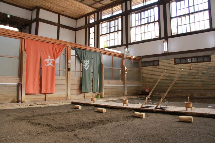 The volcanic sand bath area of Takegawara Onsen, with wooden platforms, sand, and separate changing curtains for men and women.