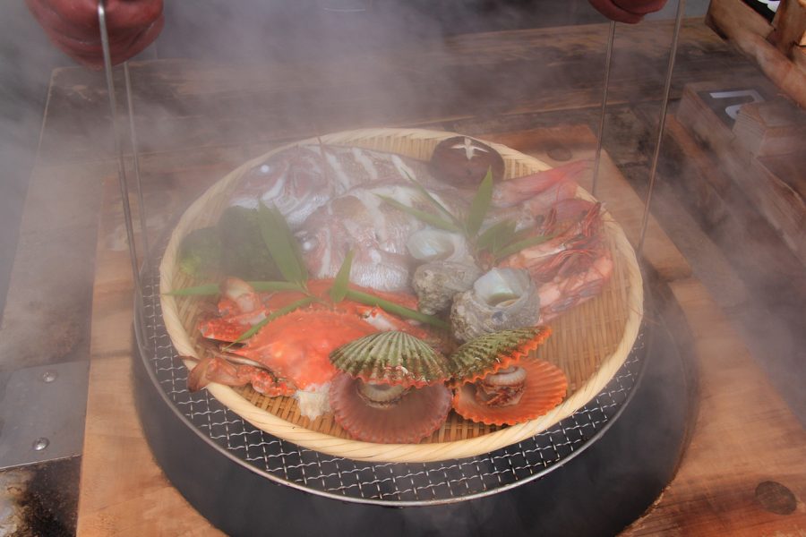 A basket of fresh seafood, including fish, crab, shrimp, and scallops, being steamed using geothermal heat (Jigokumushi cooking).