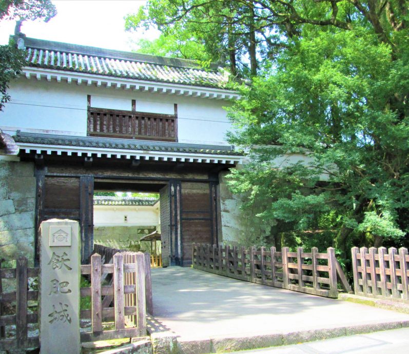 The reconstructed main gate (likely Otemon) of Obi Castle, featuring white walls, a wooden turret, and a stone pillar with Japanese characters.