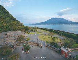 An elevated view of Sengan-en Garden and buildings, with the open water of Kagoshima Bay and the Sakurajima volcano in the distance at sunset.