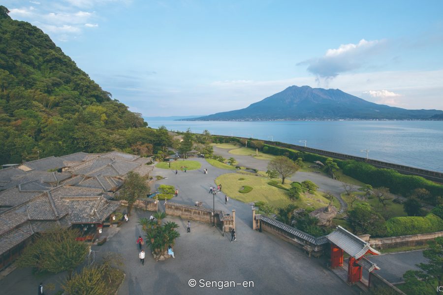 An elevated view of Sengan-en Garden and buildings, with the open water of Kagoshima Bay and the Sakurajima volcano in the distance at sunset.