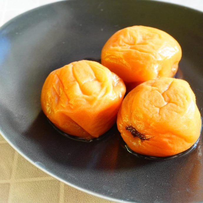 Three pickled ume plums on a black plate.