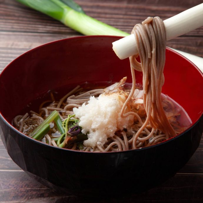 Soba noodles being lifted from a red bowl.