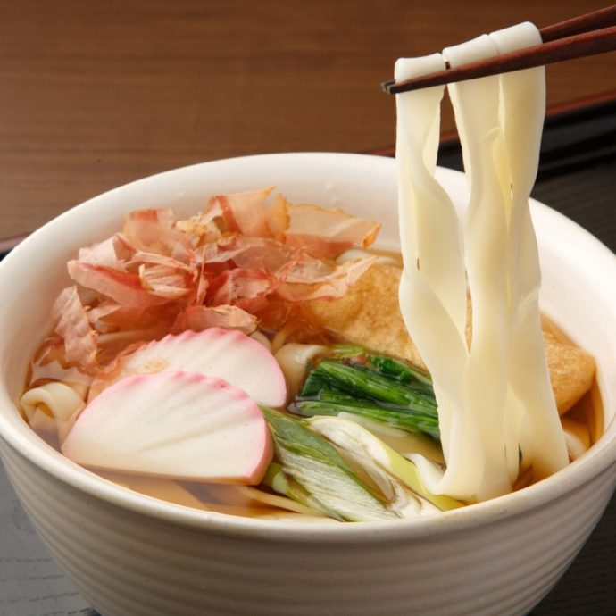 Kishimen (flat noodles) being lifted with chopsticks.