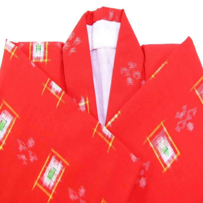 Close-up of a bright red kimono fabric with white and yellow geometric kasuri (ikat) patterns, showing the folded collar portion with a white lining.