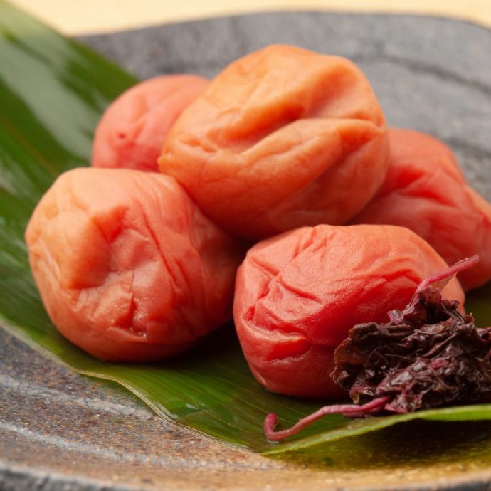 Pickled umeboshi plums on a green leaf.
