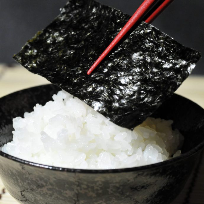 Placing a sheet of nori seaweed on white rice.