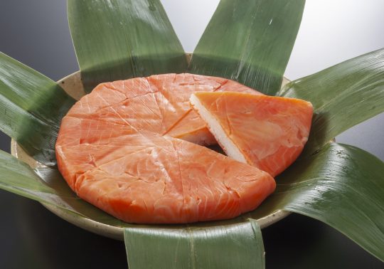 Masu-zushi (Trout Sushi). A round, pressed sushi topped with slices of salt-cured trout, wrapped in green bamboo leaves. It is cut into wedges like a pizza for serving.