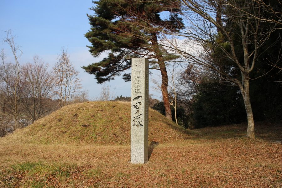 Stone monument standing in front of a preserved grassy mound of an Ichirizuka distance marker.