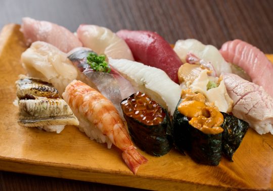 Assorted Nigiri Sushi served on a wooden plate. The selection includes tuna (maguro), sea urchin (uni), salmon roe (ikura), shrimp, eel (anago), and various white fish.