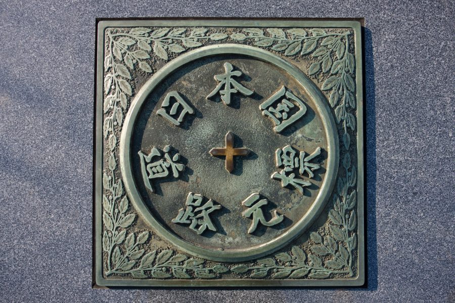 Close-up of the bronze "Kilometer Zero" marker of Japan featuring Japanese calligraphy and a floral border.